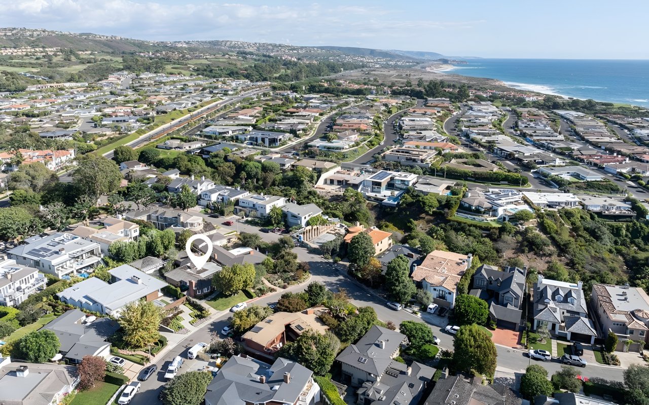  An aerial view of a coastal suburban neighborhood with a white house marked with a pin, near the ocean.