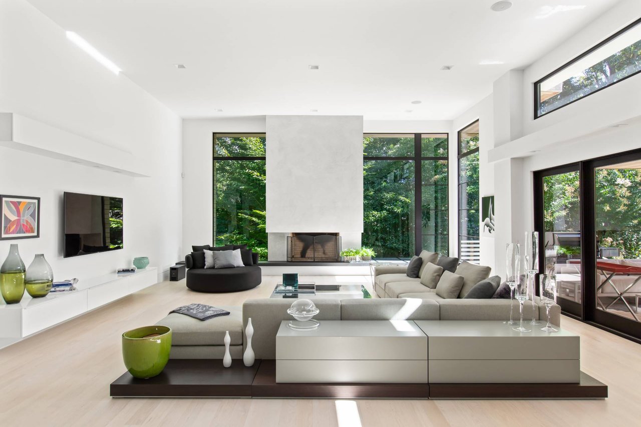 Contemporary living room with a central fireplace, tree-facing windows, and a large sectional sofa.