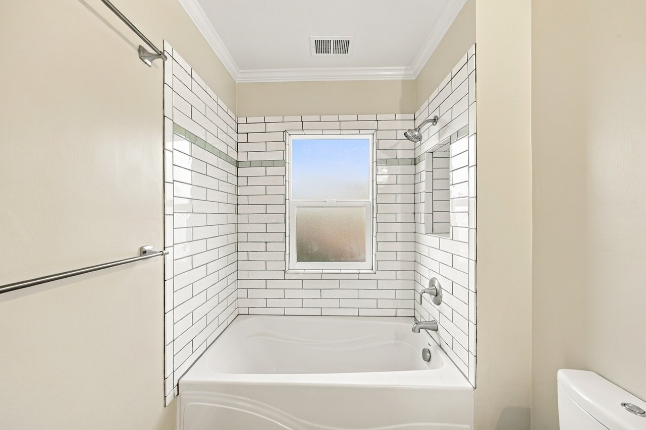 Bathroom tub and shower with white subway tile, green accent stripe, and frosted window.
