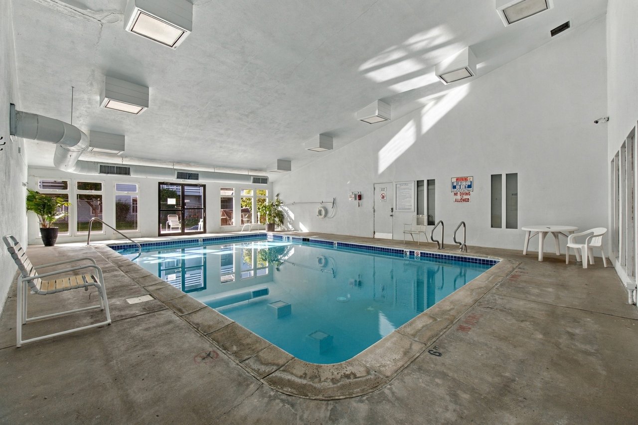 Indoor swimming pool with blue water, tiled edges, and lounge chairs along the deck.