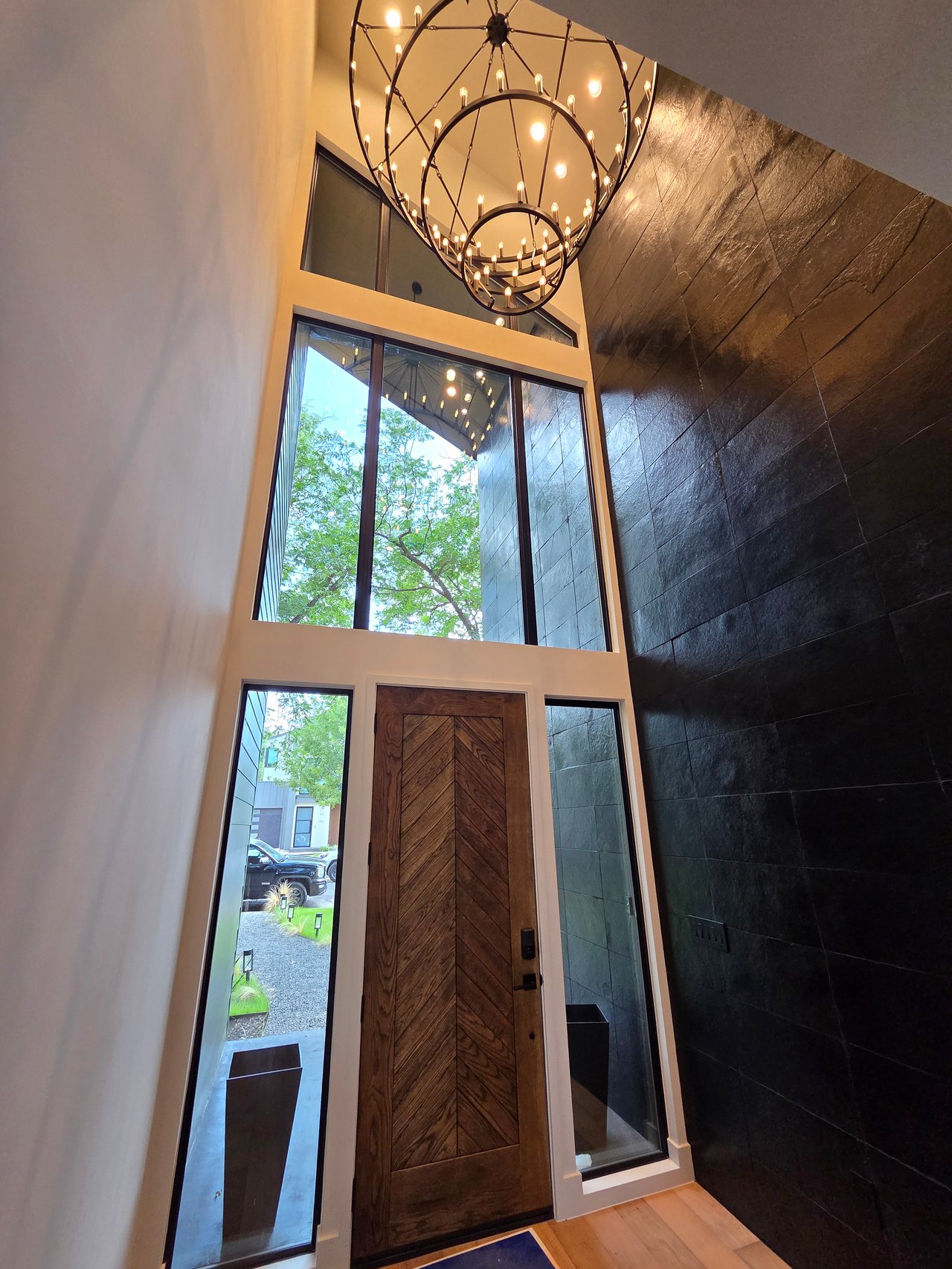 Contemporary entry foyer with a chevron wood door, dark tiled wall, and oversized circular chandelier.