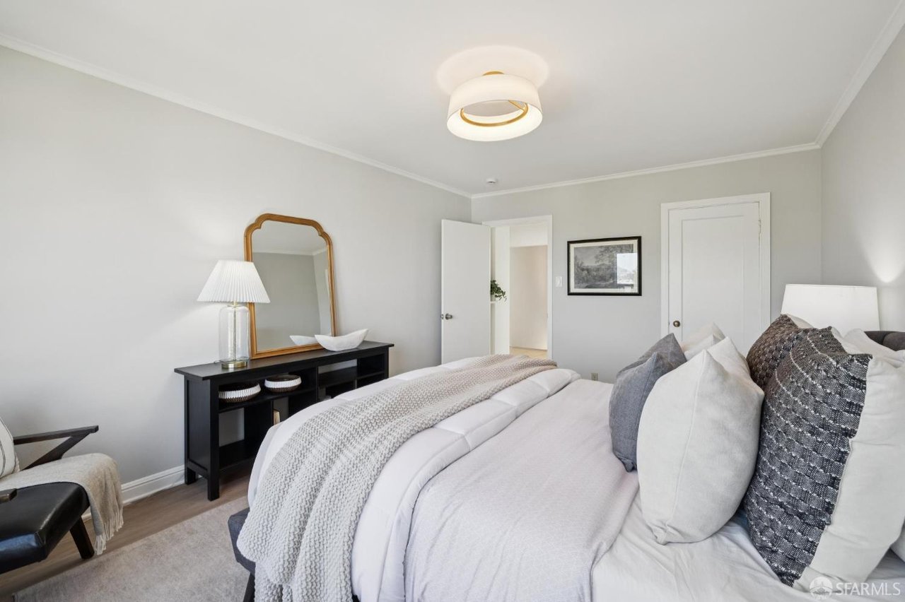 Staged bedroom with white bedding, gray accent pillows, and an arched mirror above a black console.