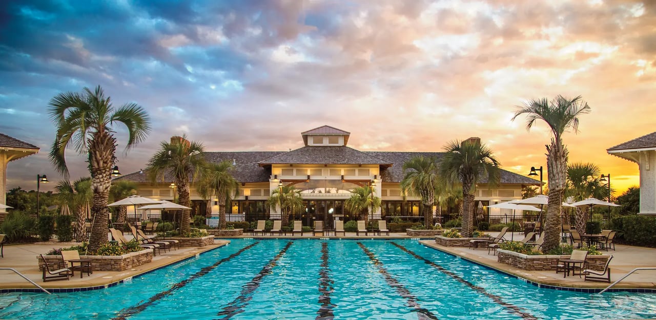 Community clubhouse behind a palm-lined outdoor swimming pool at sunset.