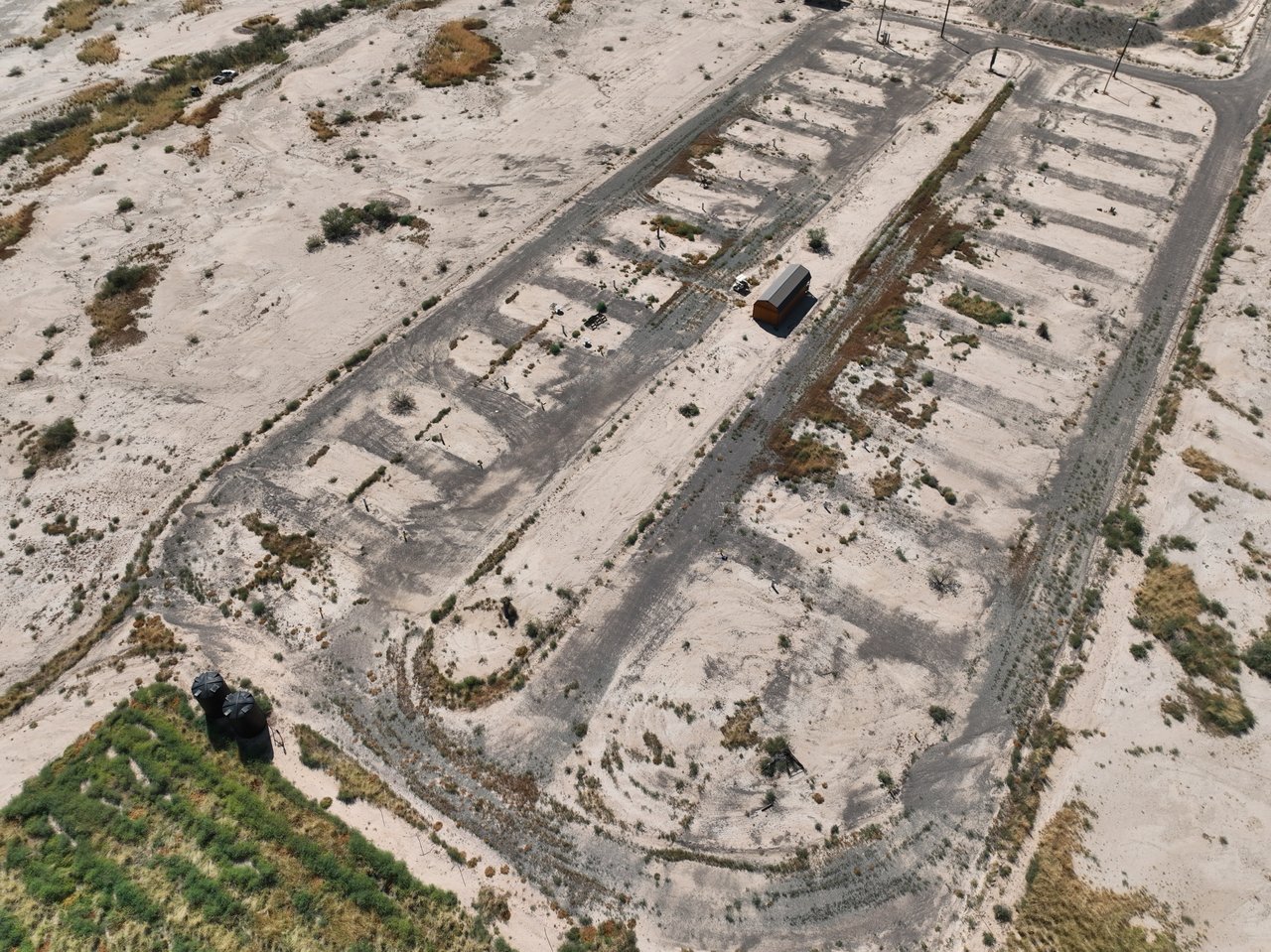 Aerial view of sandy land with graded tracks, a small shed, and two storage tanks.