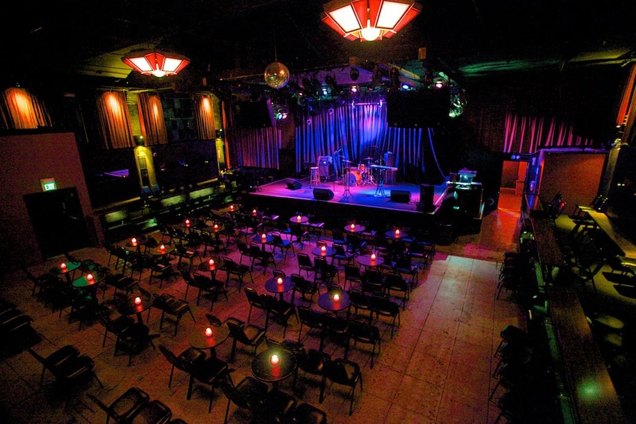 Dark concert venue with purple stage lighting and seated table arrangement
