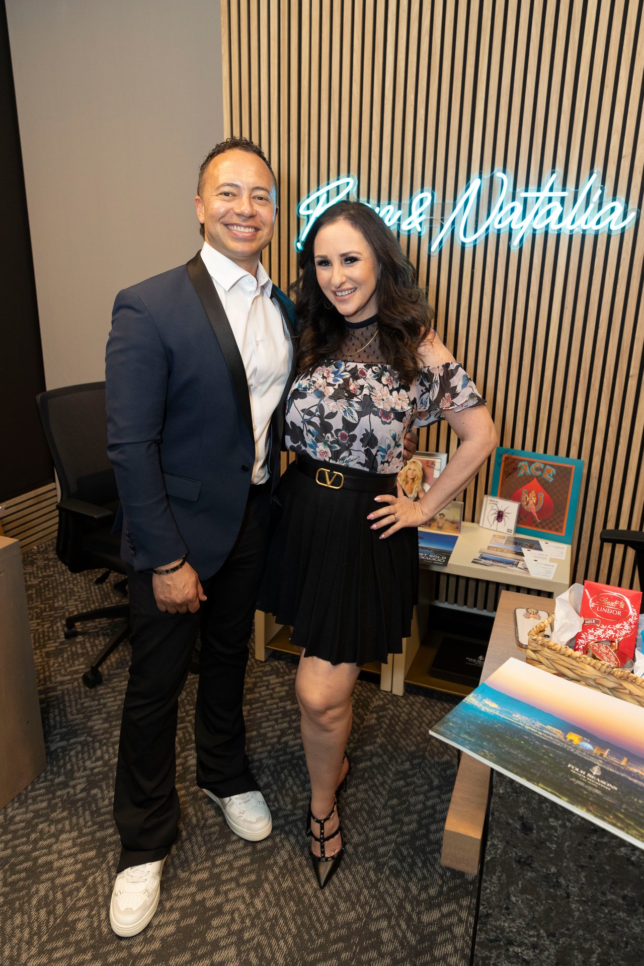 A man and woman pose beneath a glowing “Paul & Natalia” sign at an indoor event.