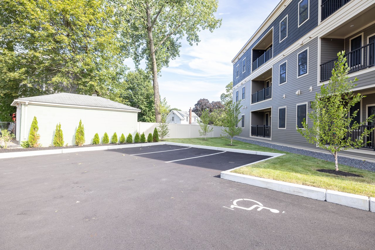 Residential building with balconies beside an accessible parking space and landscaped lawn.