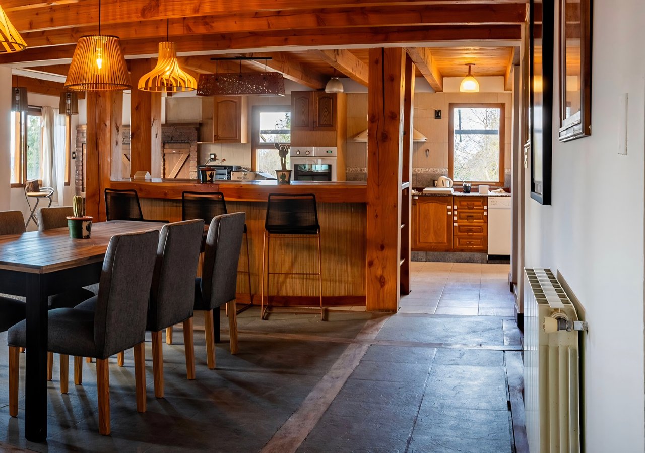Hotel boutique dining area with a wooden table, upholstered chairs, timber bar, and open kitchen.