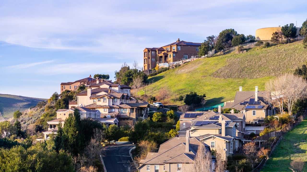 Hillside homes in Hayward beside a winding street and green slopes.