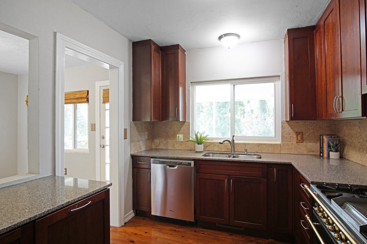 Bright kitchen with dark wood cabinets, granite countertops, stainless steel appliances, and a window above the sink. A potted plant adds freshness.