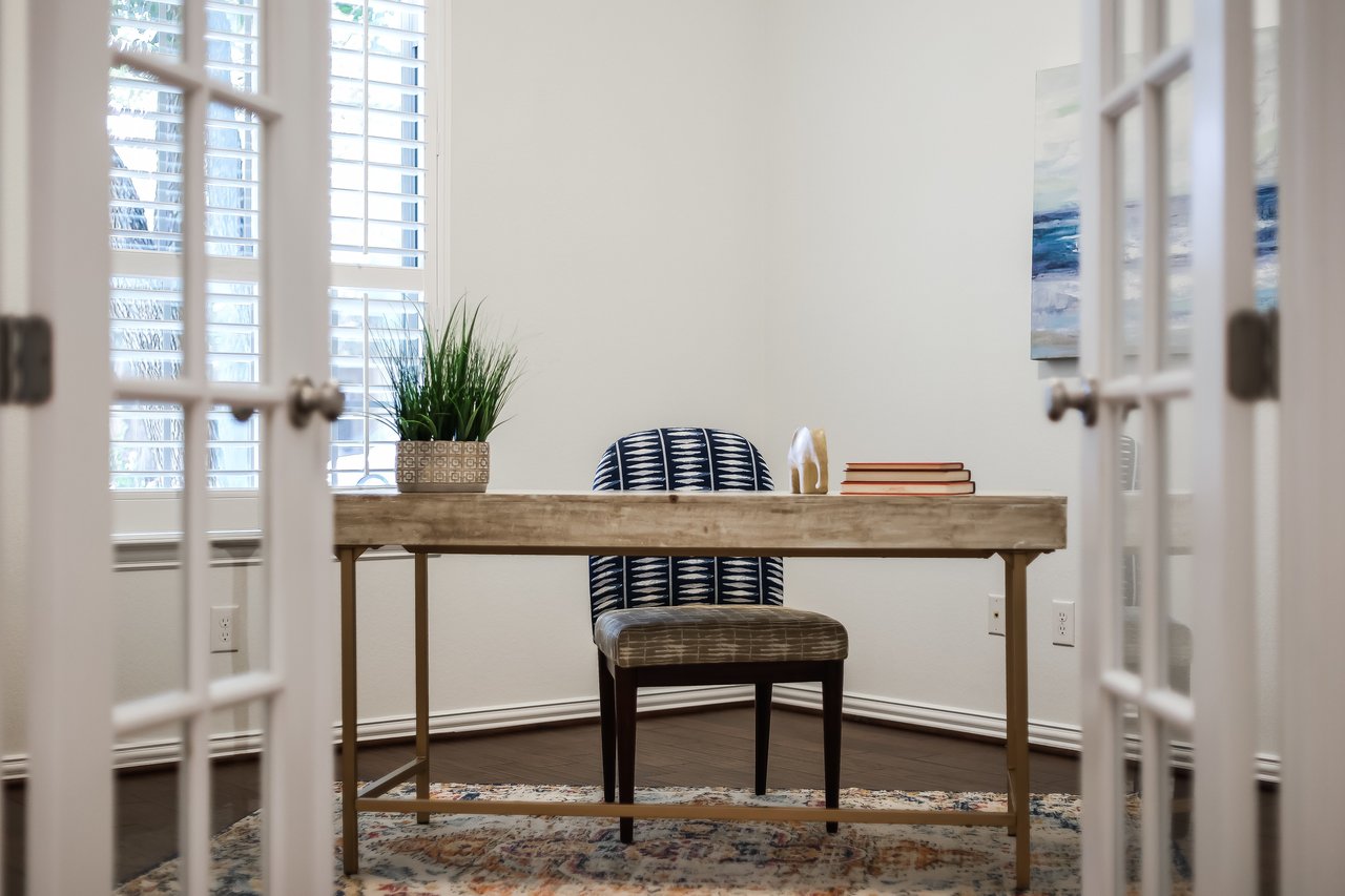 Furnished home office with a wooden desk, patterned chair, and shuttered windows.