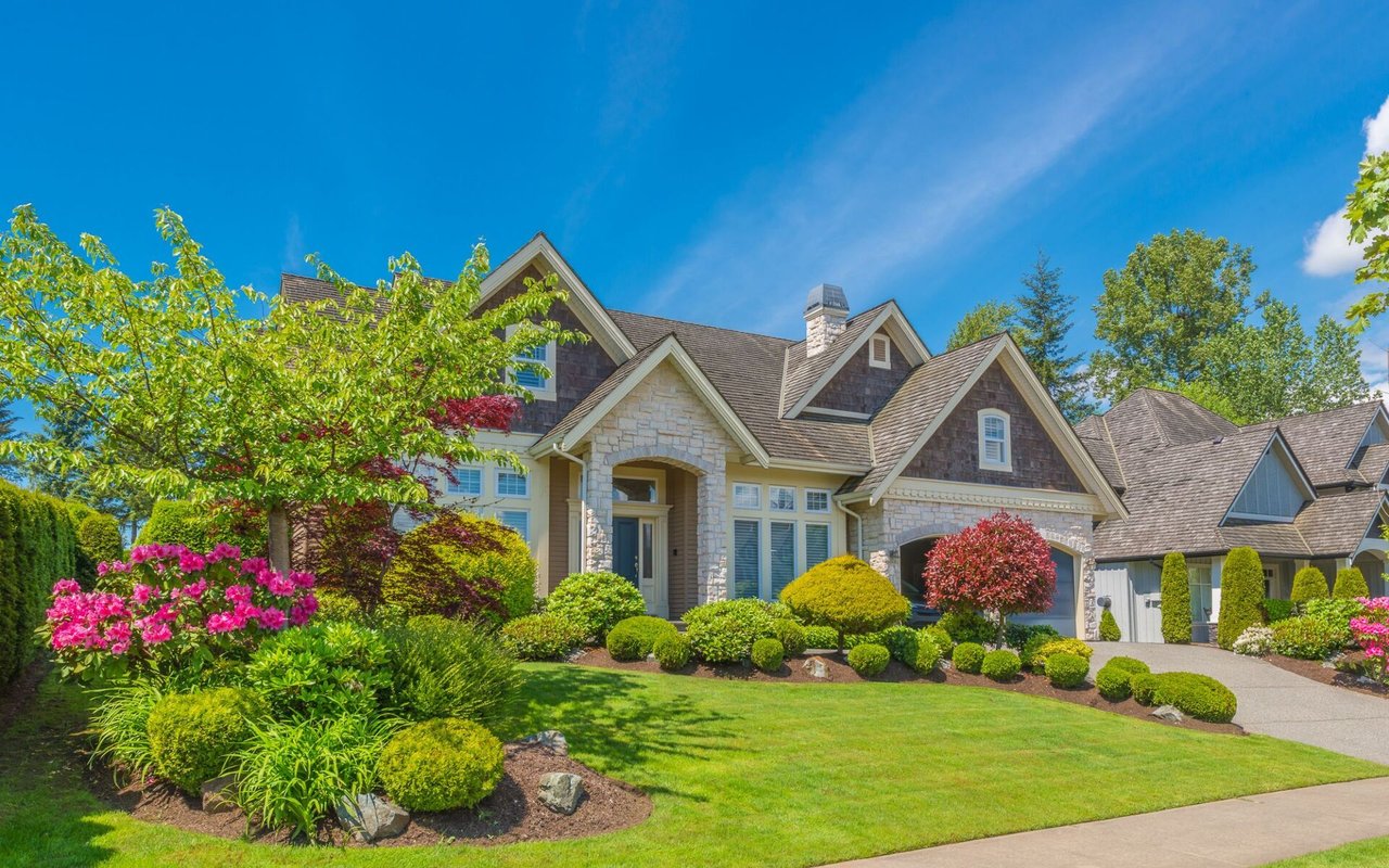 Stone-fronted home with multiple gables, colorful landscaping, a broad lawn, and a driveway.
