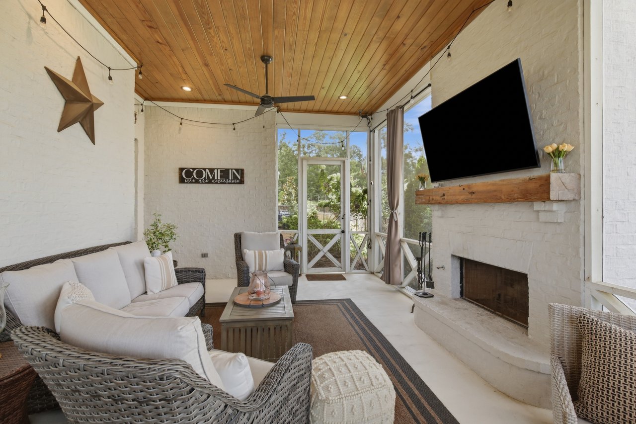 Sunroom with wicker seating, a wood-plank ceiling, and a white brick fireplace.