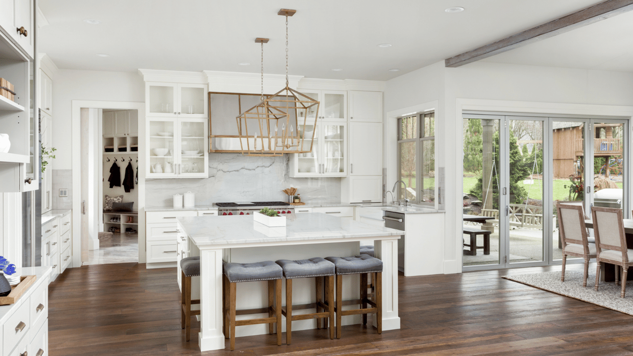 Bright white kitchen with a marble island, gray stools, brass pendant lights, and sliding doors to a patio.