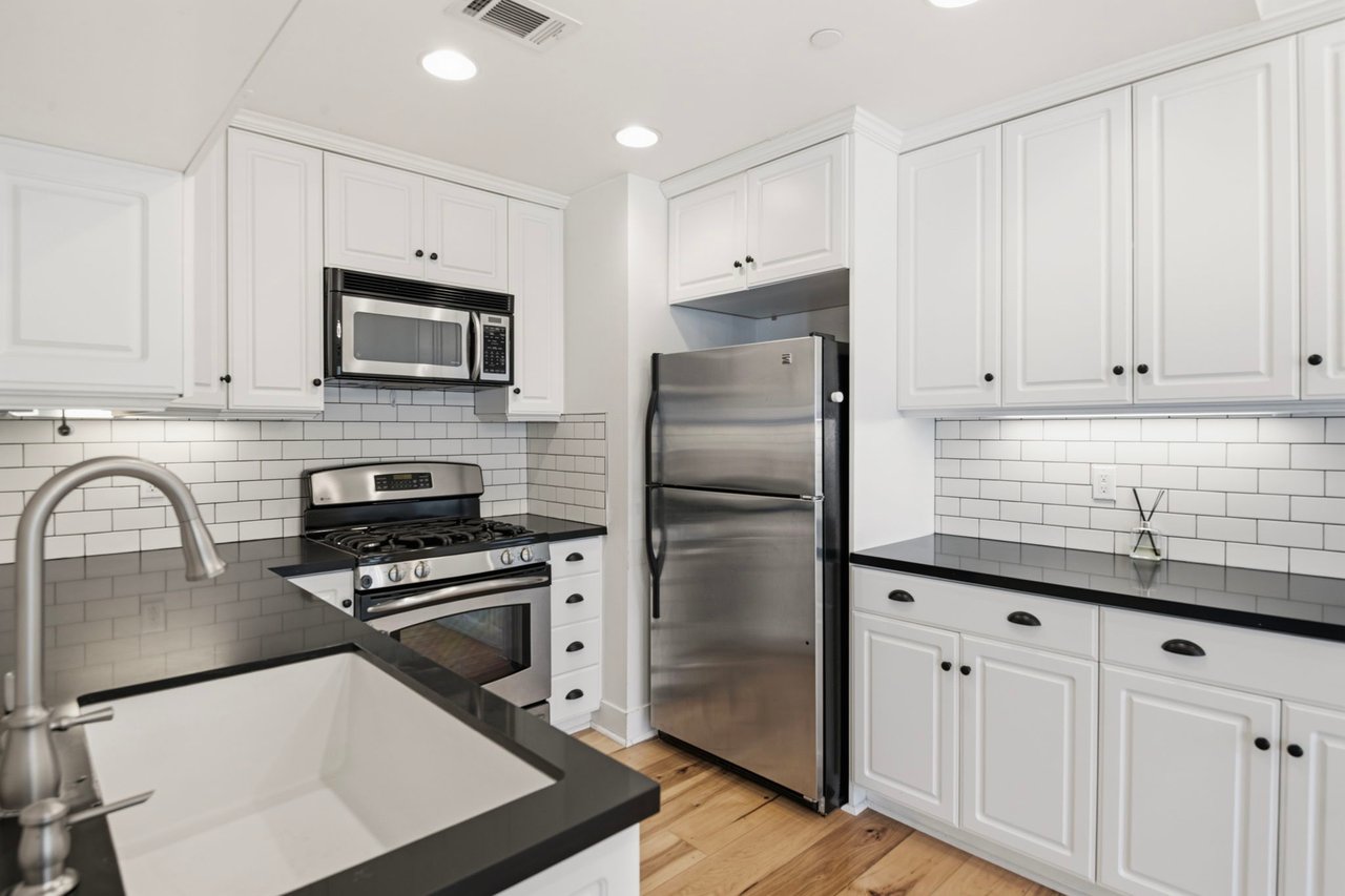 Kitchen peninsula with sink, dark countertops, and stainless steel appliances surrounded by white cabinetry