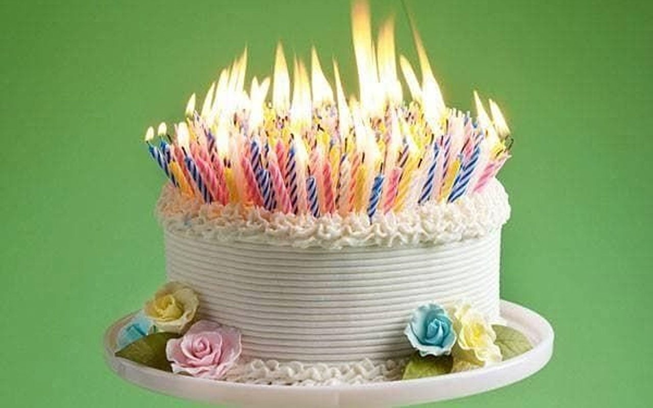 White birthday cake topped with colorful lit candles and pastel sugar roses.