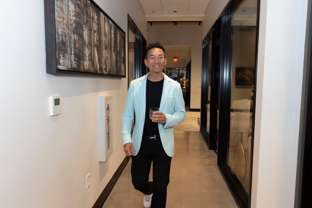 Man in a light blue blazer holding a drink in a modern office hallway