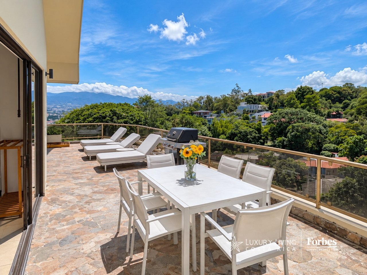 Penthouse terrace with outdoor dining and lounge furniture overlooking green hills and distant mountains.