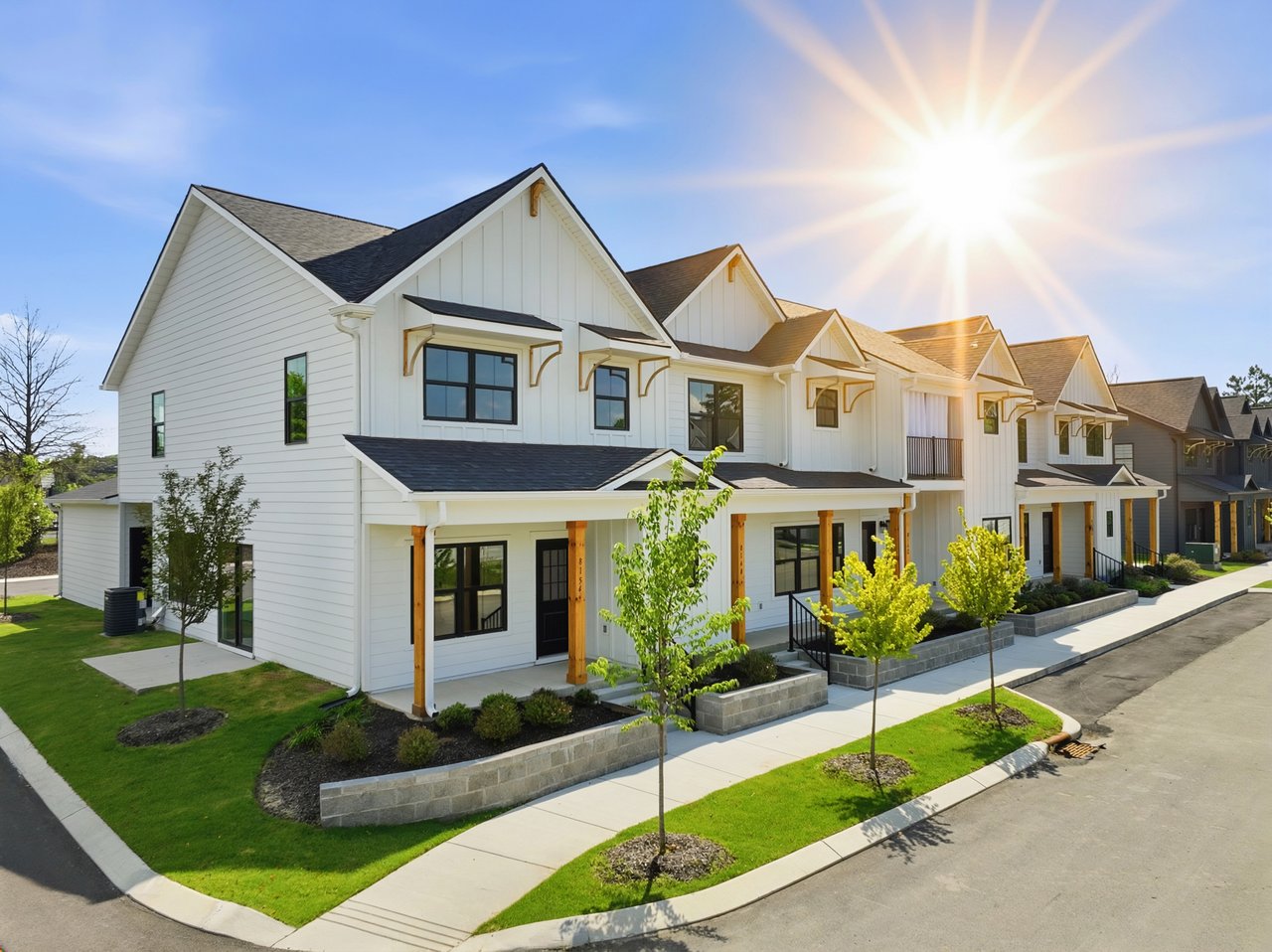 Row of white modern townhomes with covered porches along a landscaped sidewalk.