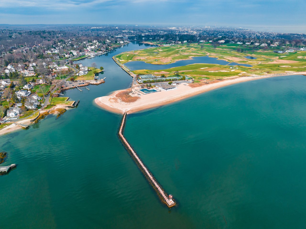 Aerial view of a coastal neighborhood with a sandy beach, waterway, and green grounds.