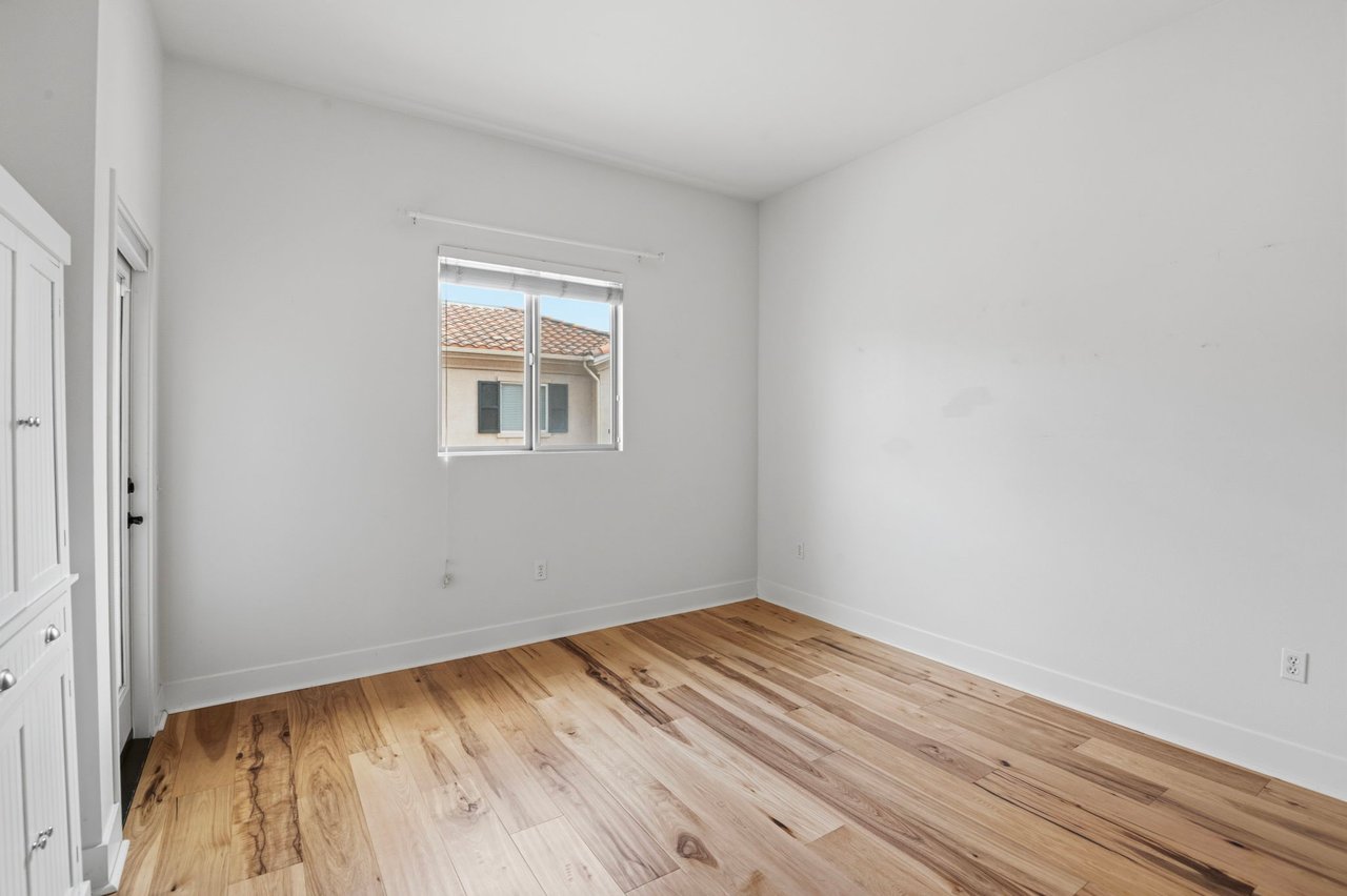 Additional bedroom with wide-plank hardwood floors, natural light from sliding window, and neutral wall tones