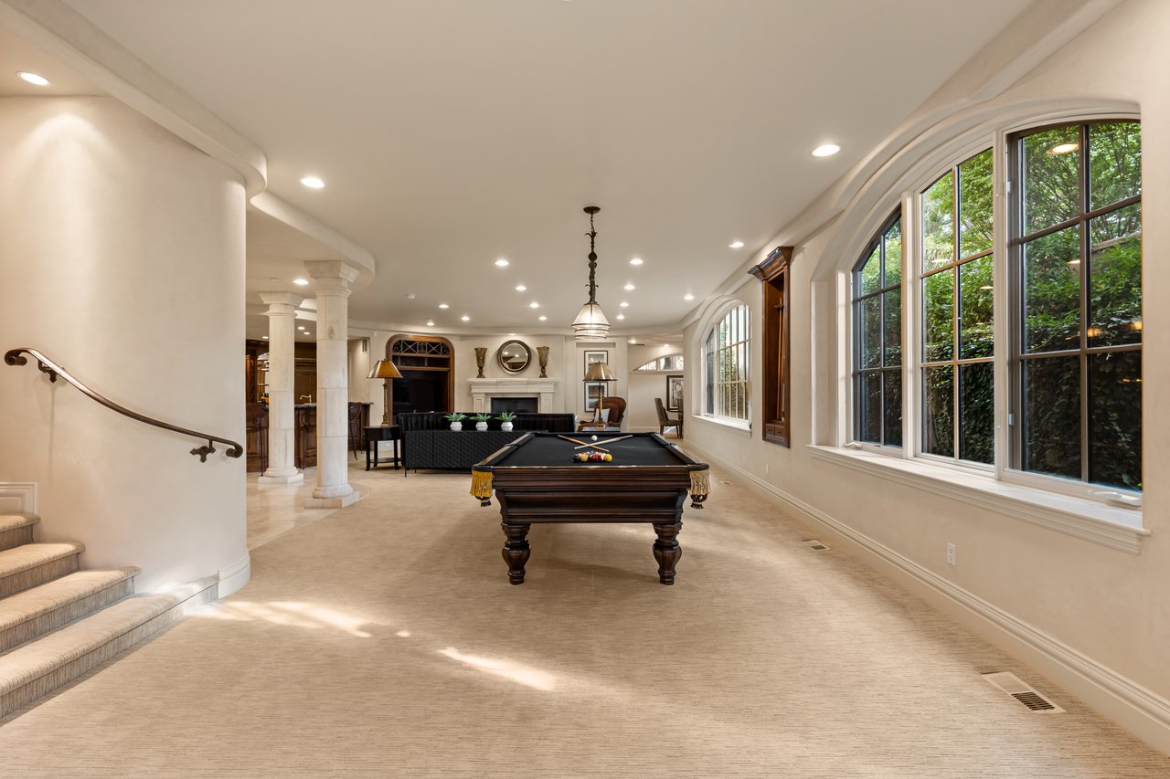 Game room with a billiards table, fireplace, marble columns, and large arched windows.