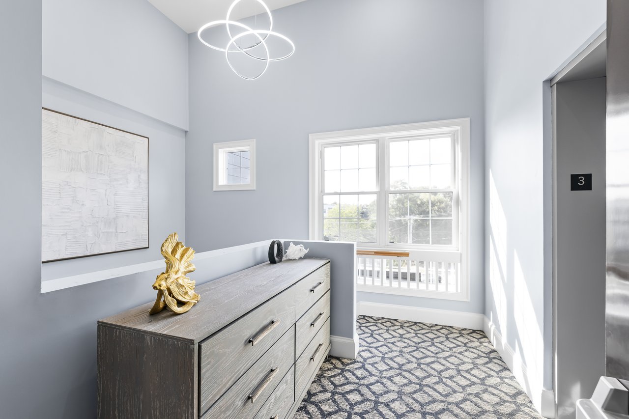 Bright interior with a gray dresser, gold fish sculpture, geometric carpet, and large windows.
