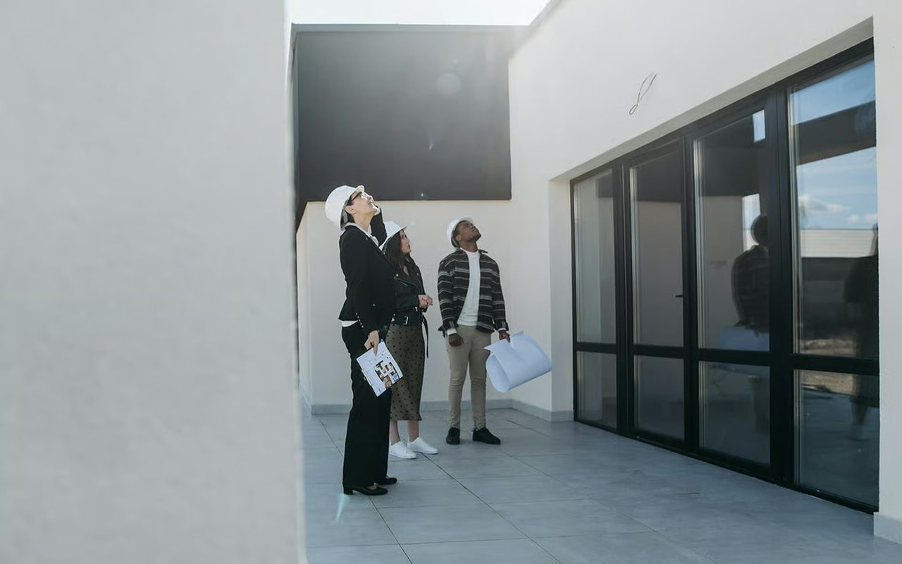 Three people inspect a modern, empty home with high ceilings and large glass doors.