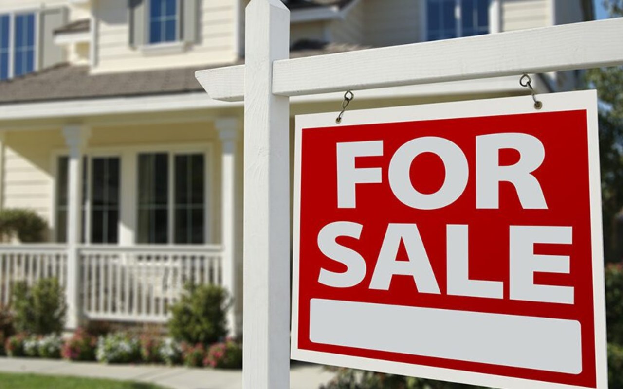 House for sale, with a prominent red sign in front of its covered porch.