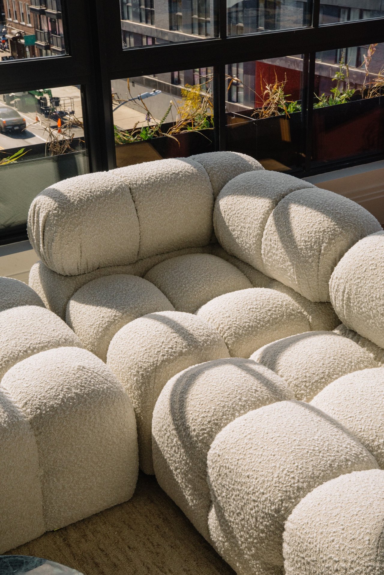 Cream bouclé sofa with rounded cushions beside large windows overlooking the city.