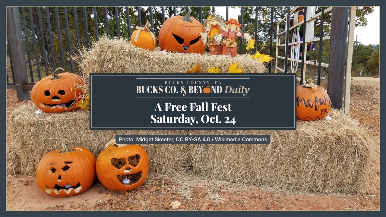 Carved and painted jack-o'-lanterns and fall leaves arranged on stacked hay bales in front of an iron fence.