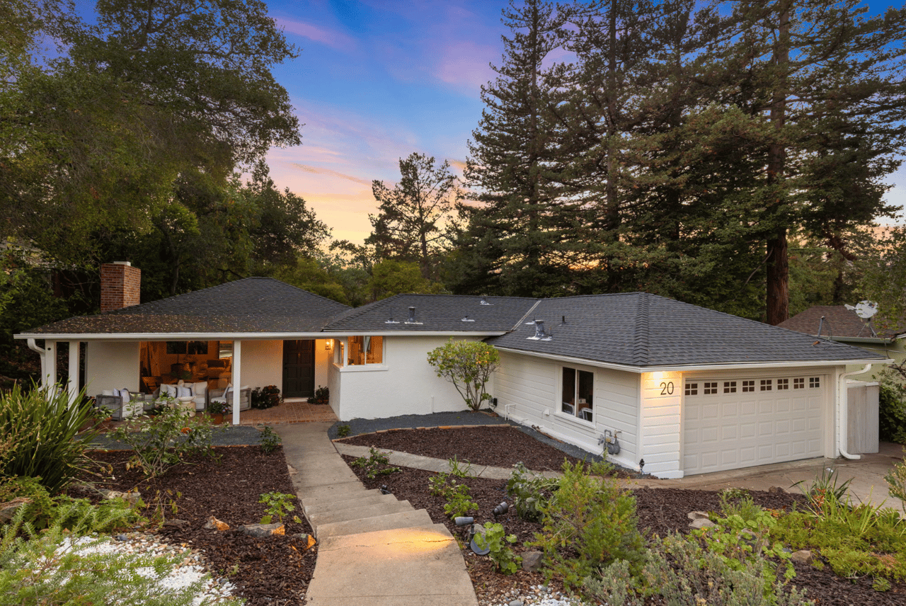 Single-story white house with a two-car garage, landscaped path, and tall trees at dusk.