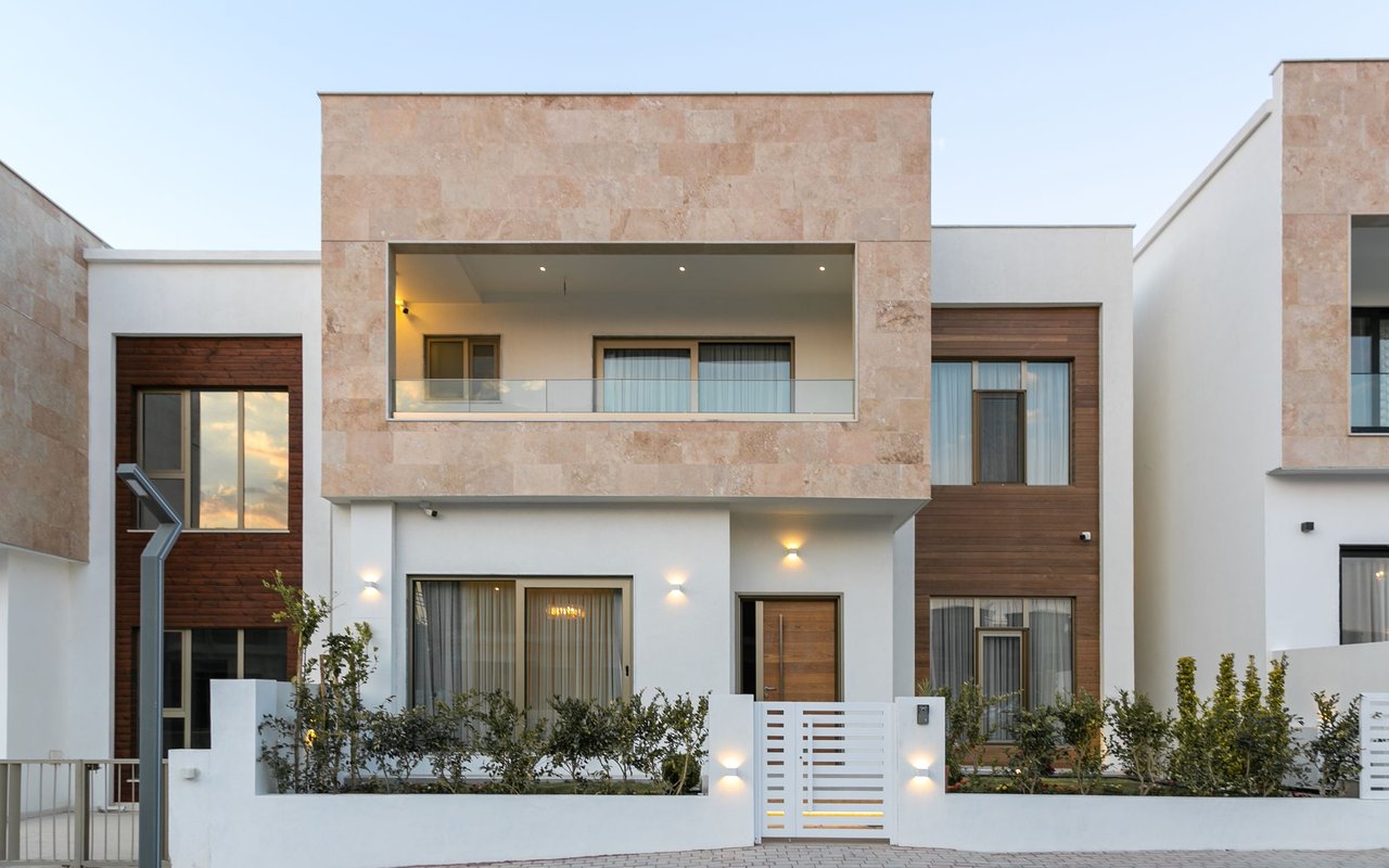 Modern two-story home with a recessed balcony, stone facade, wood accents, and gated front yard.