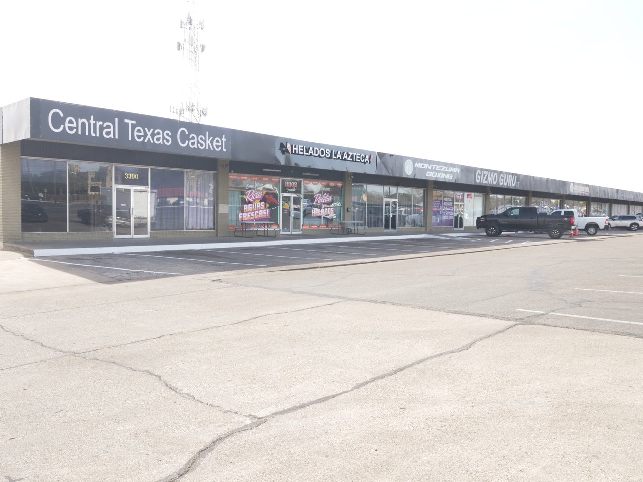 Commercial strip center with multiple storefronts and a parking lot in front.