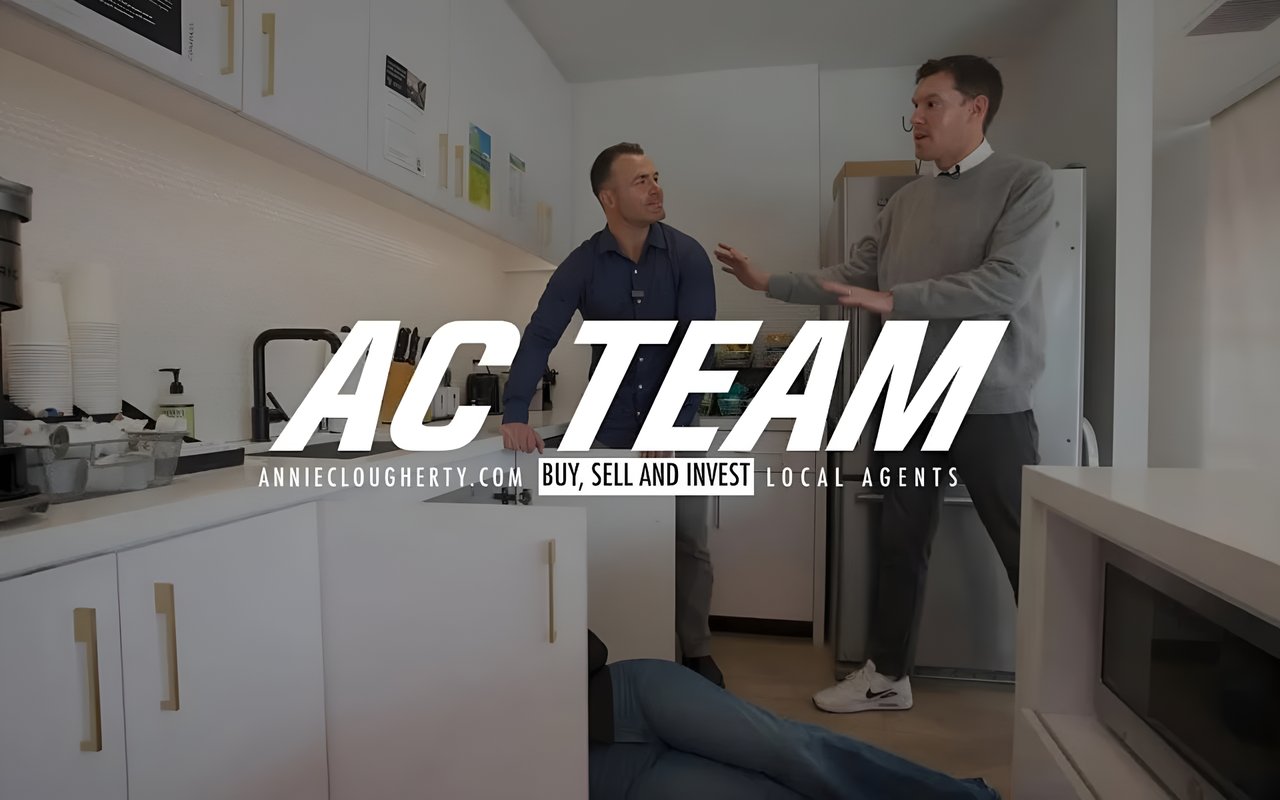  A team of two real estate professionals, one in a blue shirt and the other in a gray sweater, stands in a modern office kitchen.
