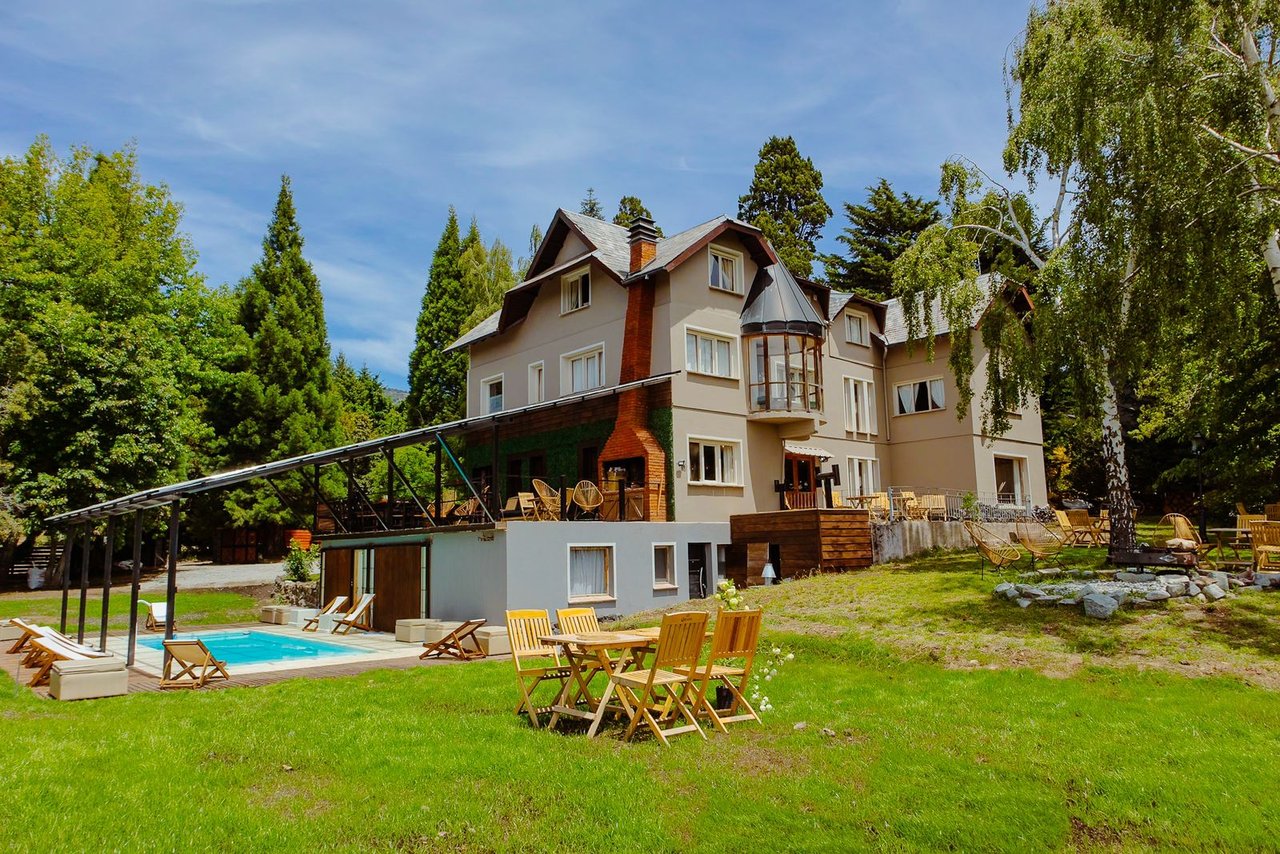 Boutique hotel with a swimming pool, covered patio, and outdoor seating on a tree-lined lawn.
