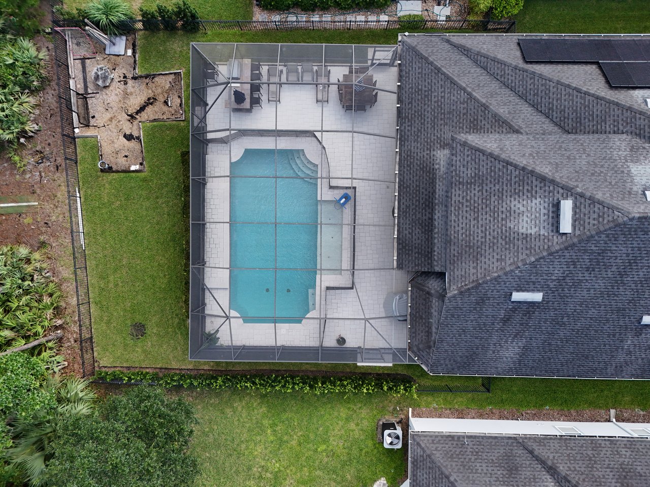 Aerial view of a screened backyard pool beside a gray-roofed home with solar panels.