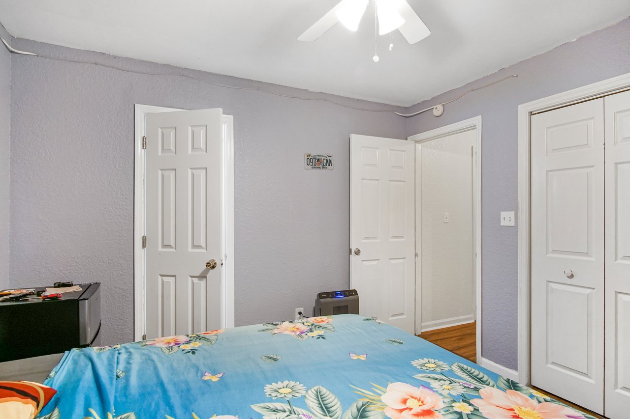 Bedroom at 2506 Nugget Lane in Tallahassee, Florida, with lavender-painted walls, ceiling fan with light, and wood-look flooring. The room includes double closet doors and multiple entry doors, providing ample storage and access.