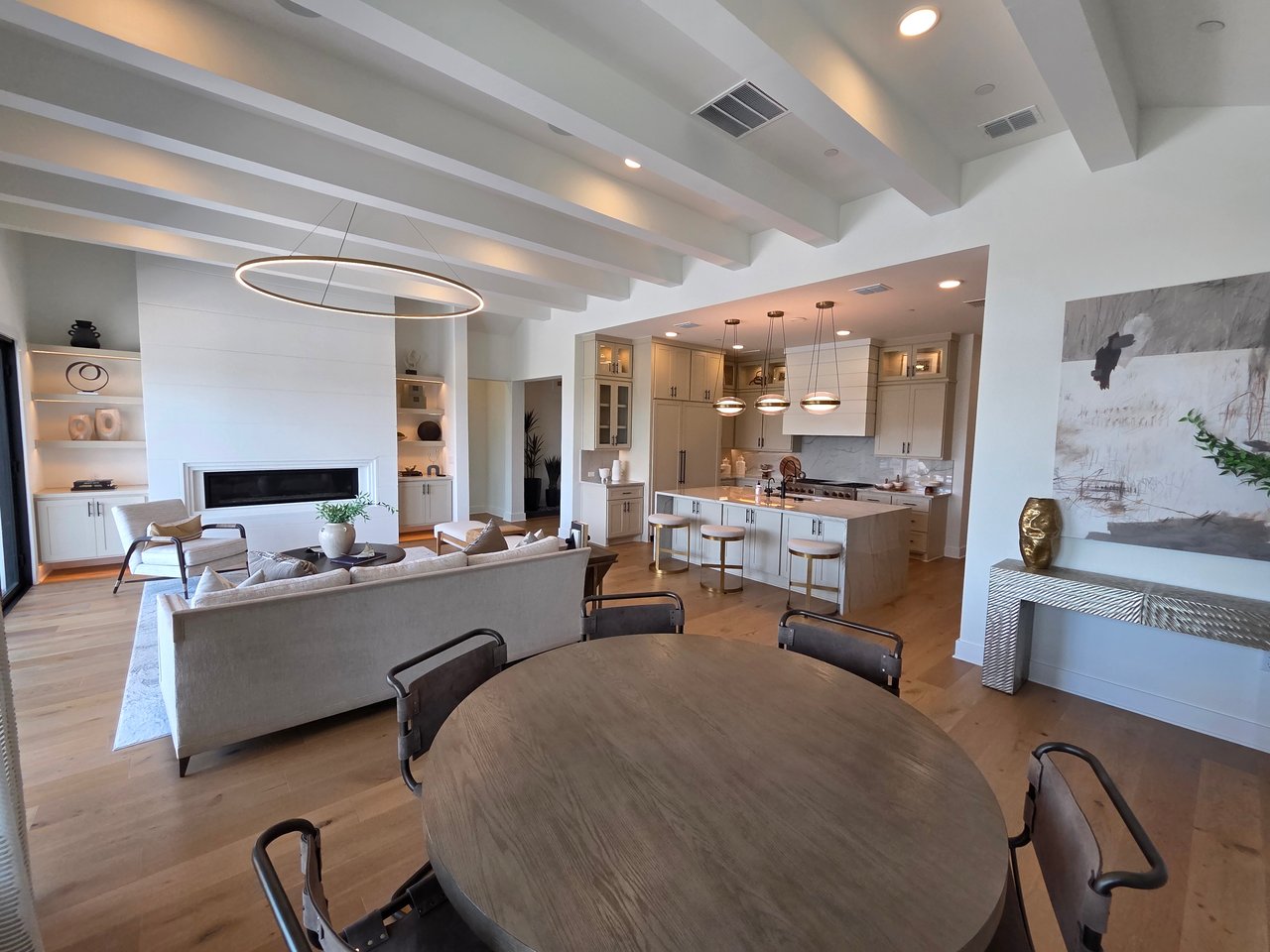 Open-plan living room and kitchen with exposed beams, a white fireplace, and a large island.