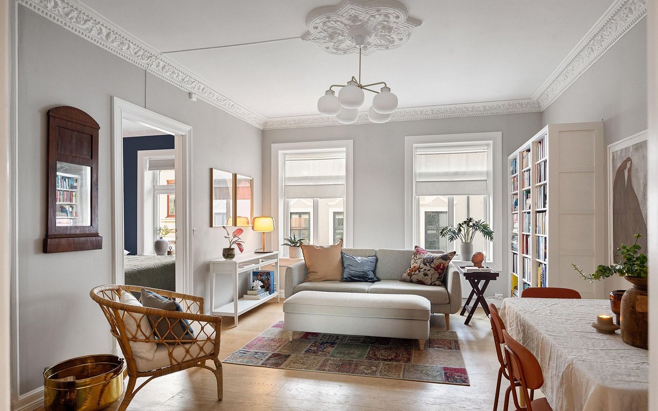 Living room with a gray sofa, wicker armchair, colorful rug, tall windows, and ornate crown molding.