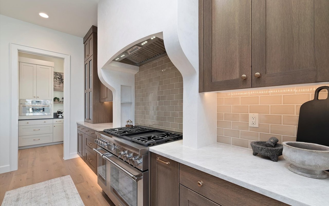 Kitchen close-up of the double oven/range with sage glass subway tile backsplash and white plaster range hood