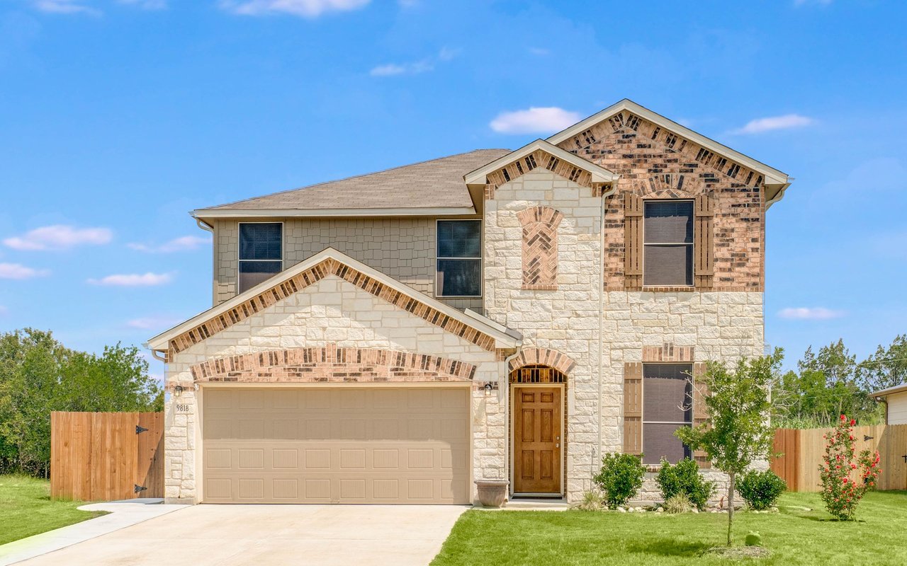Two-story stone-and-brick home with a two-car garage, wooden entry door, and fenced lawn.