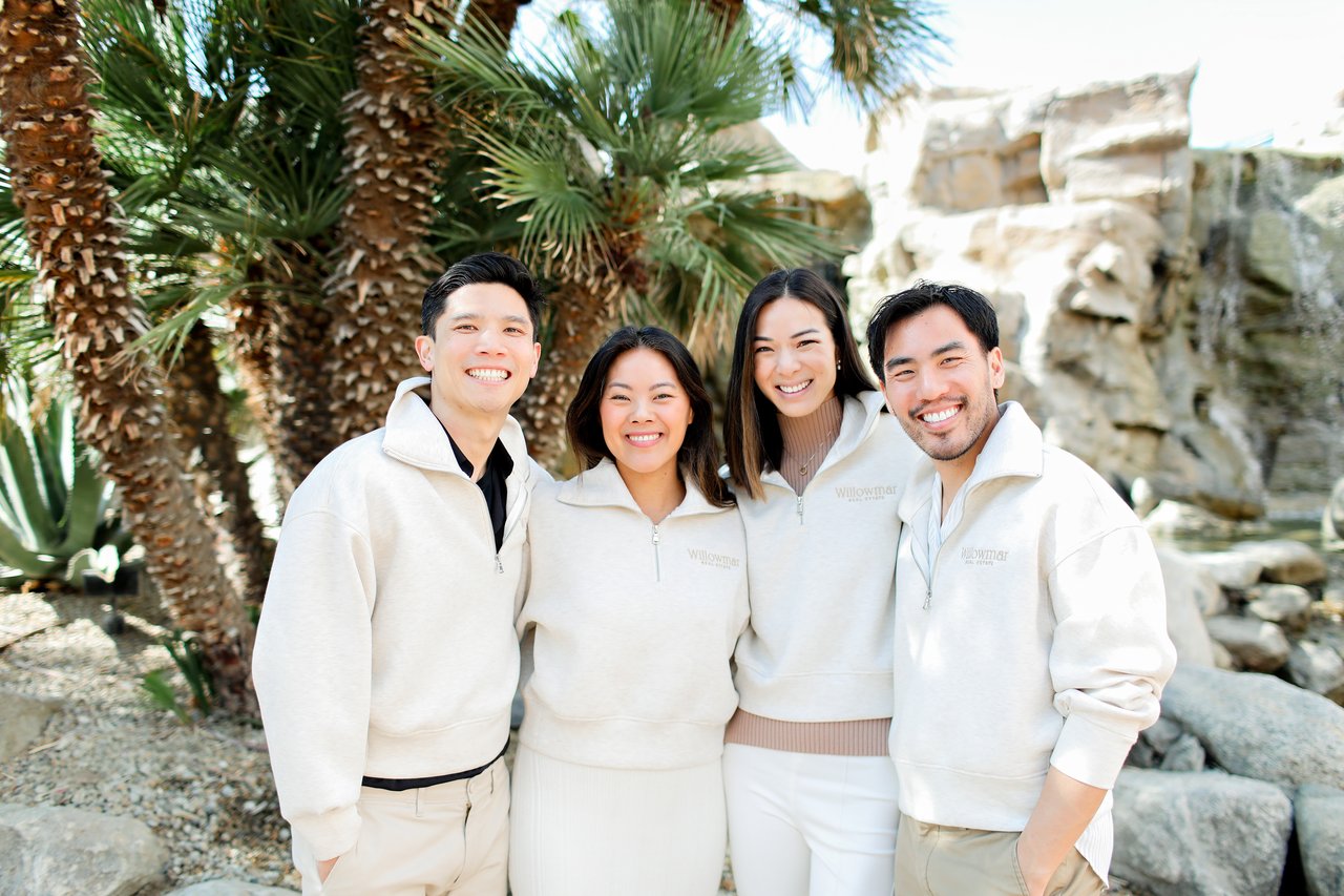 Four Willowmar team members pose in light-colored sweatshirts among palm trees and rocks.