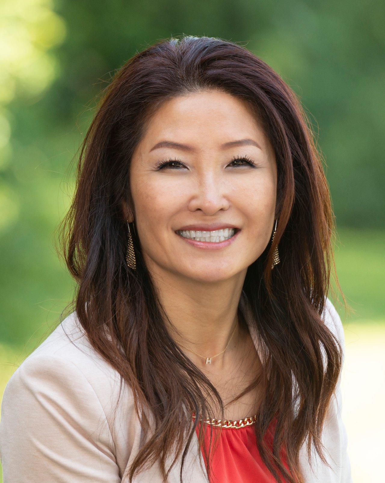 Julie Pae smiling in a white blazer and red top outdoors.