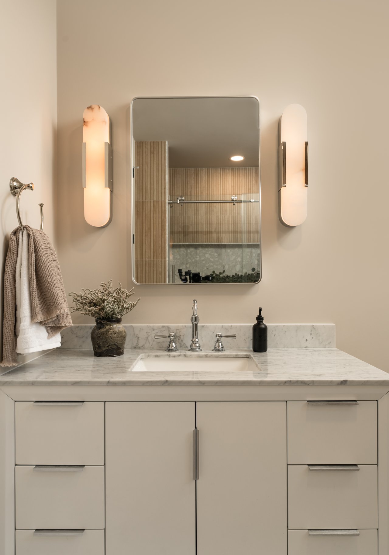 Bathroom vanity with marble counter, chrome faucet, framed mirror, and warm wall sconces.