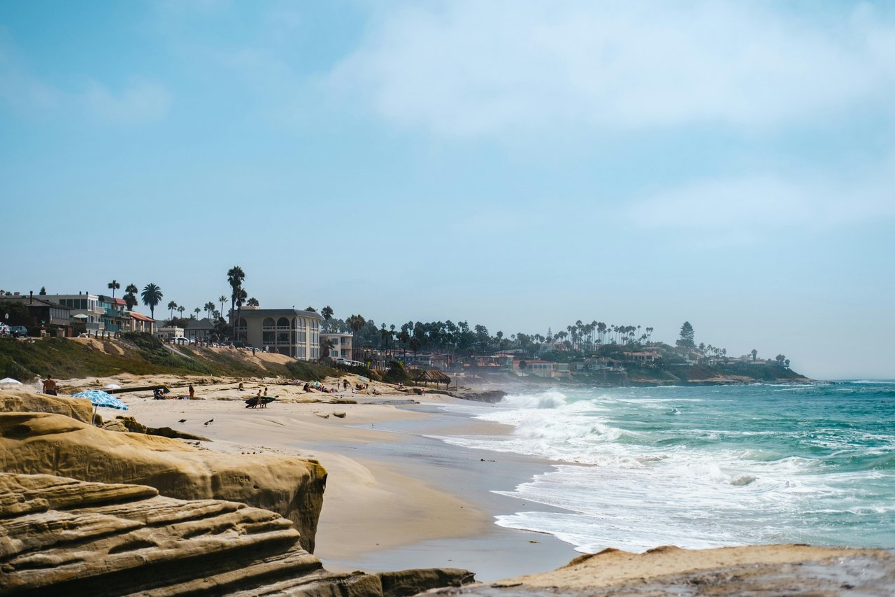 Surfer and beachgoers on La Jolla beach with palm trees and oceanfront buildings in the background