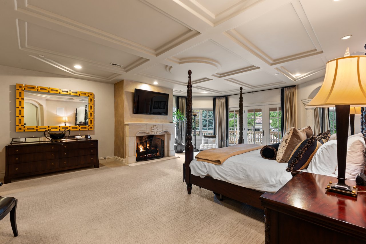 Furnished bedroom with a carved four-poster bed, fireplace, coffered ceiling, and balcony doors.