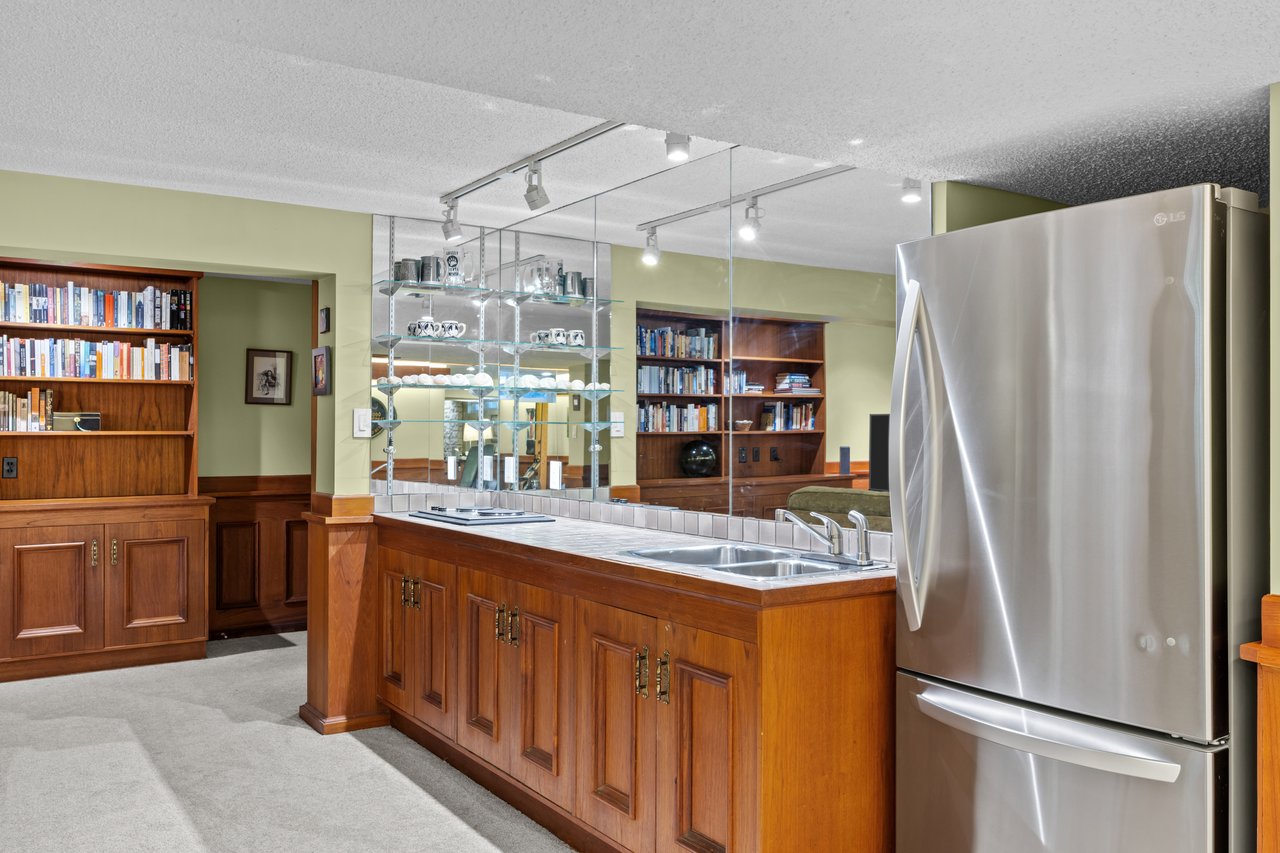 Kitchen with a wood-paneled island, mirrored backsplash, bookshelves, and stainless steel refrigerator.