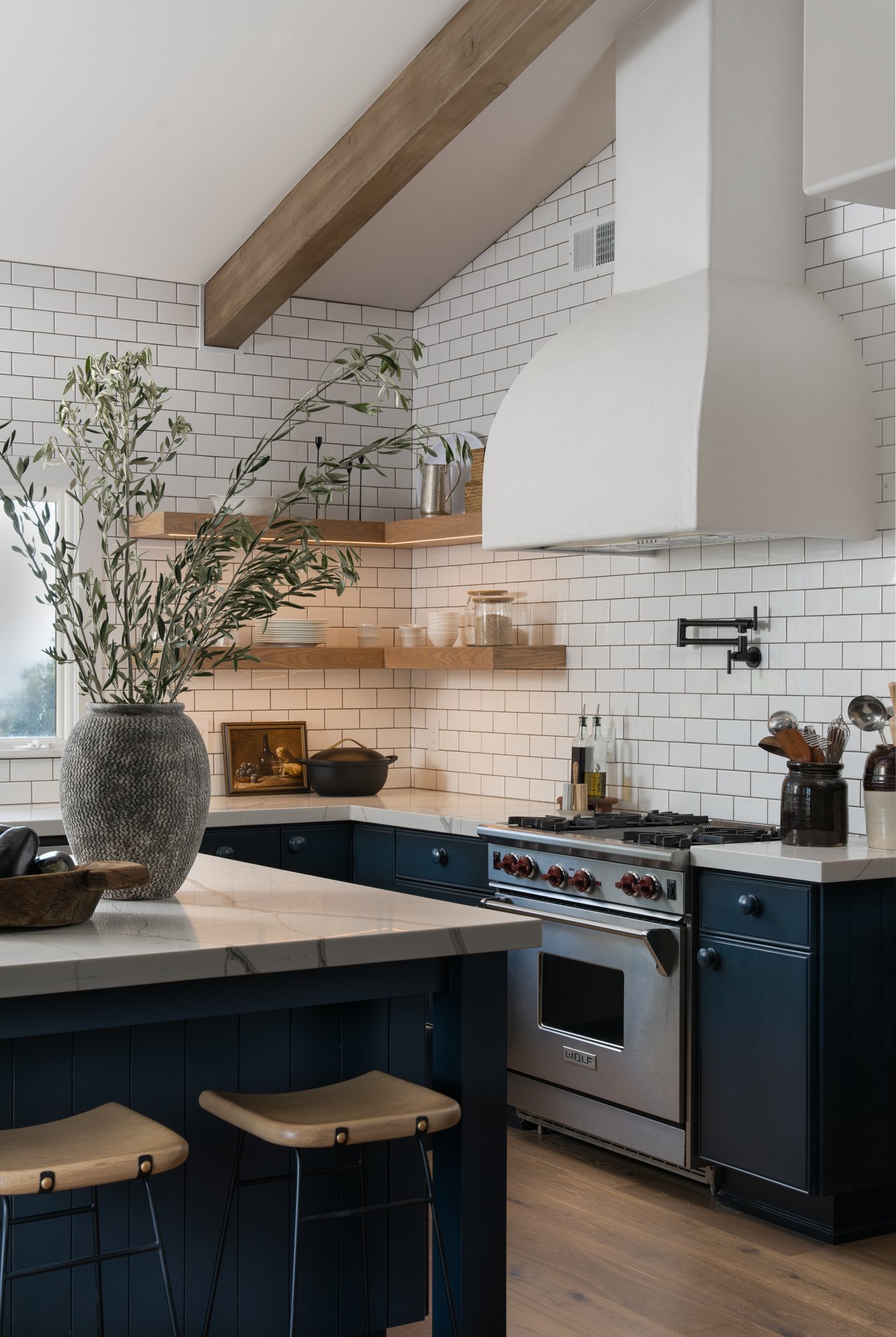 Kitchen with white subway tile, navy cabinets, a marble island, and a stainless-steel range.