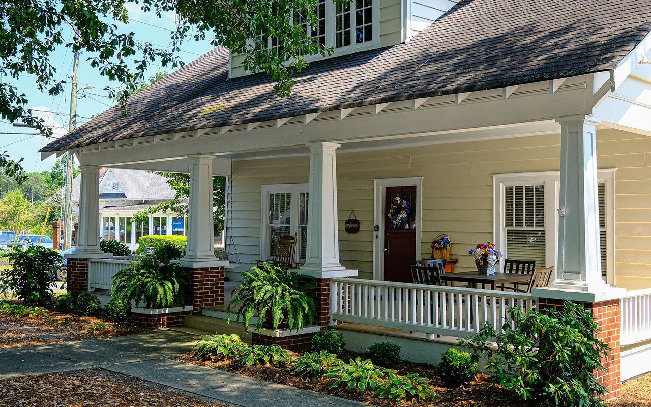 House with a deep covered porch, white columns, brick bases, and outdoor seating.